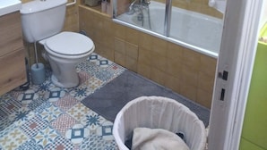 Un baño con inodoro, lavamanos, ducha y piso estampado.