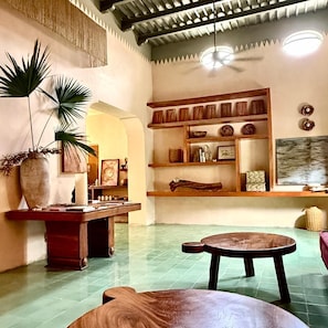 Una habitación con suelo de baldosas, un banco de madera, una mesa con un jarrón y estanterías con adornos.