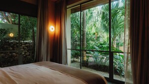 Un dormitorio con una cama grande, una pared de piedra y vistas a exuberante vegetación a través de amplios ventanales correderos.