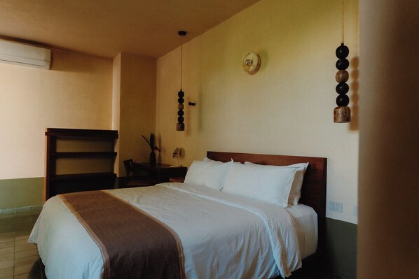 A neatly made bed with white linens, a wooden headboard, and a hanging wooden decoration. - Casa Querida (Mérida)
