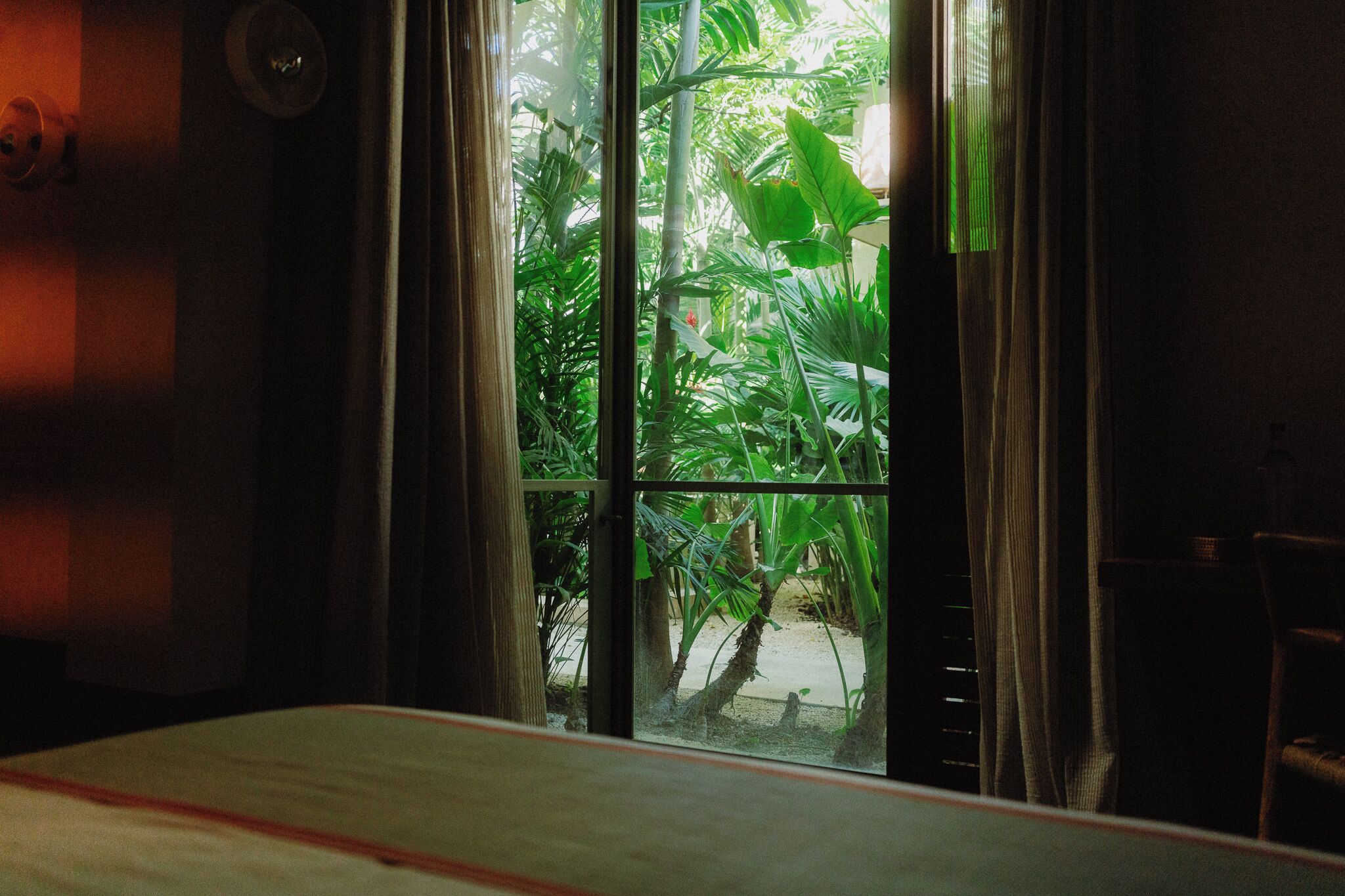 Une chambre avec un lit, une fenêtre avec des rideaux et une vue sur la verdure.