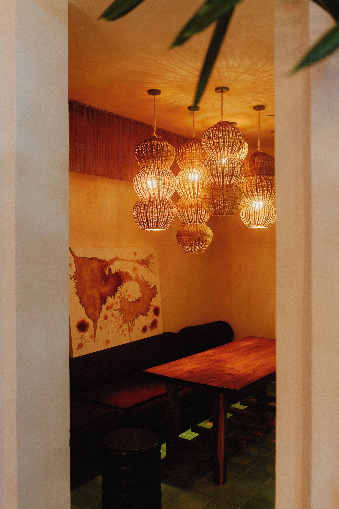 A dining area with a wooden table and chairs, a wall with a textured mural, and multiple hanging wicker-style pendant lights.