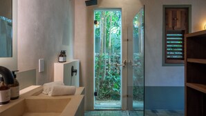 Un baño moderno con bañera, cabina de ducha de vidrio y vistas a la vegetación exterior.