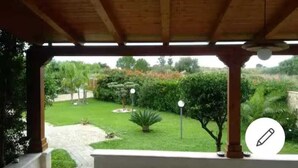 A covered patio with a view of a well-maintained garden. - Adonai House (Sicilia)