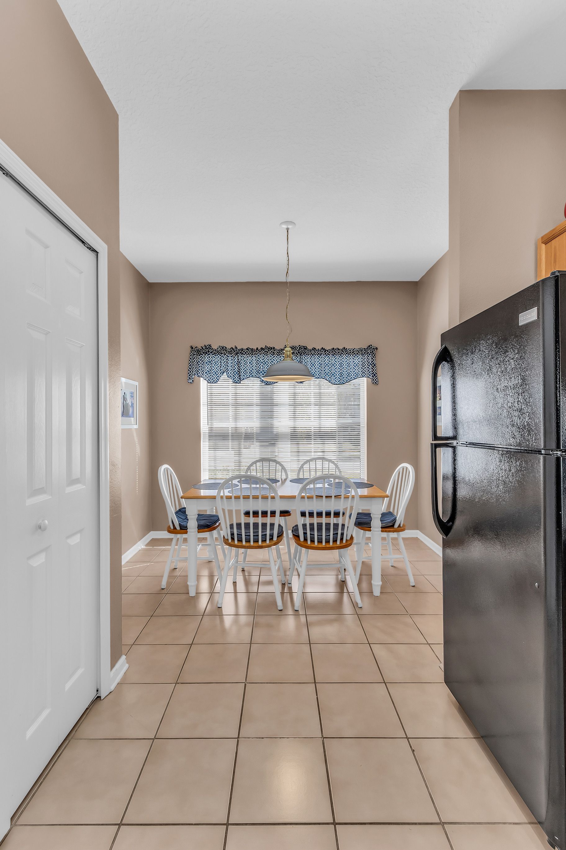 A kitchen with a dining table, chairs, a refrigerator, and a window with blinds.
