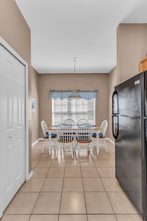 A kitchen with a dining table, chairs, a refrigerator, and a window with blinds. - Disney Getaway - Private Pool & Resort Amenities (Kissimmee)