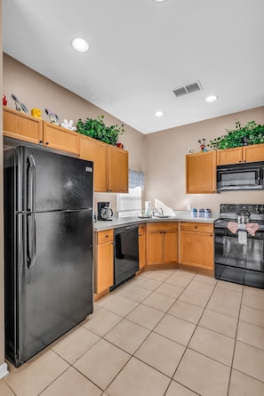 A modern kitchen with a black refrigerator, wooden cabinets, a microwave, and a stove. - Disney Getaway - Private Pool & Resort Amenities (Kissimmee)
