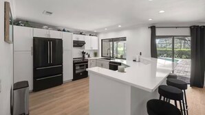 Une cuisine moderne avec des meubles blancs, des appareils électroménagers noirs et un grand îlot central doté de tabourets de bar.