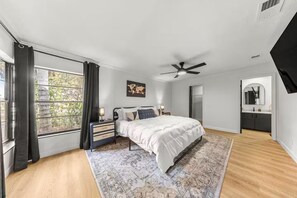 A bedroom with a bed, bedside tables, a ceiling fan, a window with curtains, and a view of the outdoors. - Citrus Hills Retreat | Pool + Golf Views (Hernando)
