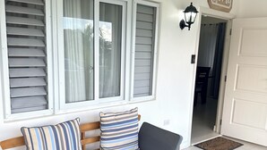 A wooden bench with cushions, a white exterior wall, and a door with a 'home' sign. - Luxury Retreat at Sorrell Ave (St Ann’s Bay)