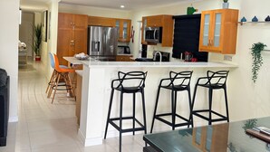 A modern kitchen with wooden cabinets, stainless steel appliances, and a large clock on the wall. - Luxury Retreat at Sorrell Ave (St Ann’s Bay)