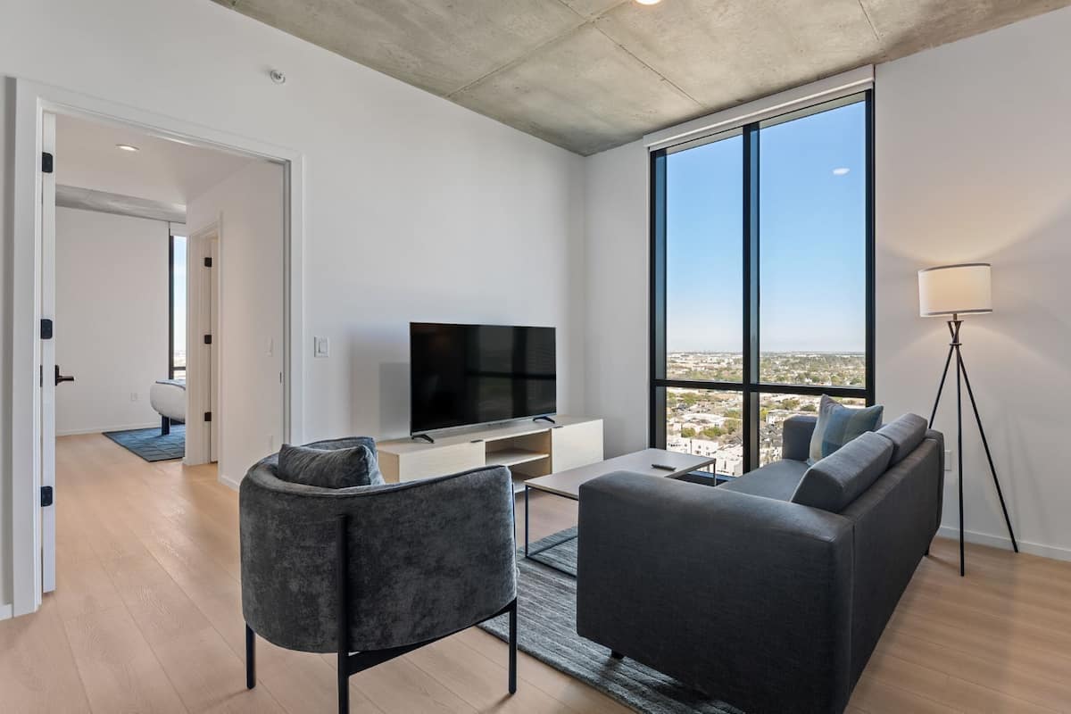 Una sala de estar moderna con un televisor de pantalla plana, un sofá gris y un ventanal con vistas a la ciudad.