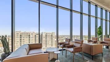 A high-rise hotel room with large windows, leather seating, a small round table, and a potted plant.