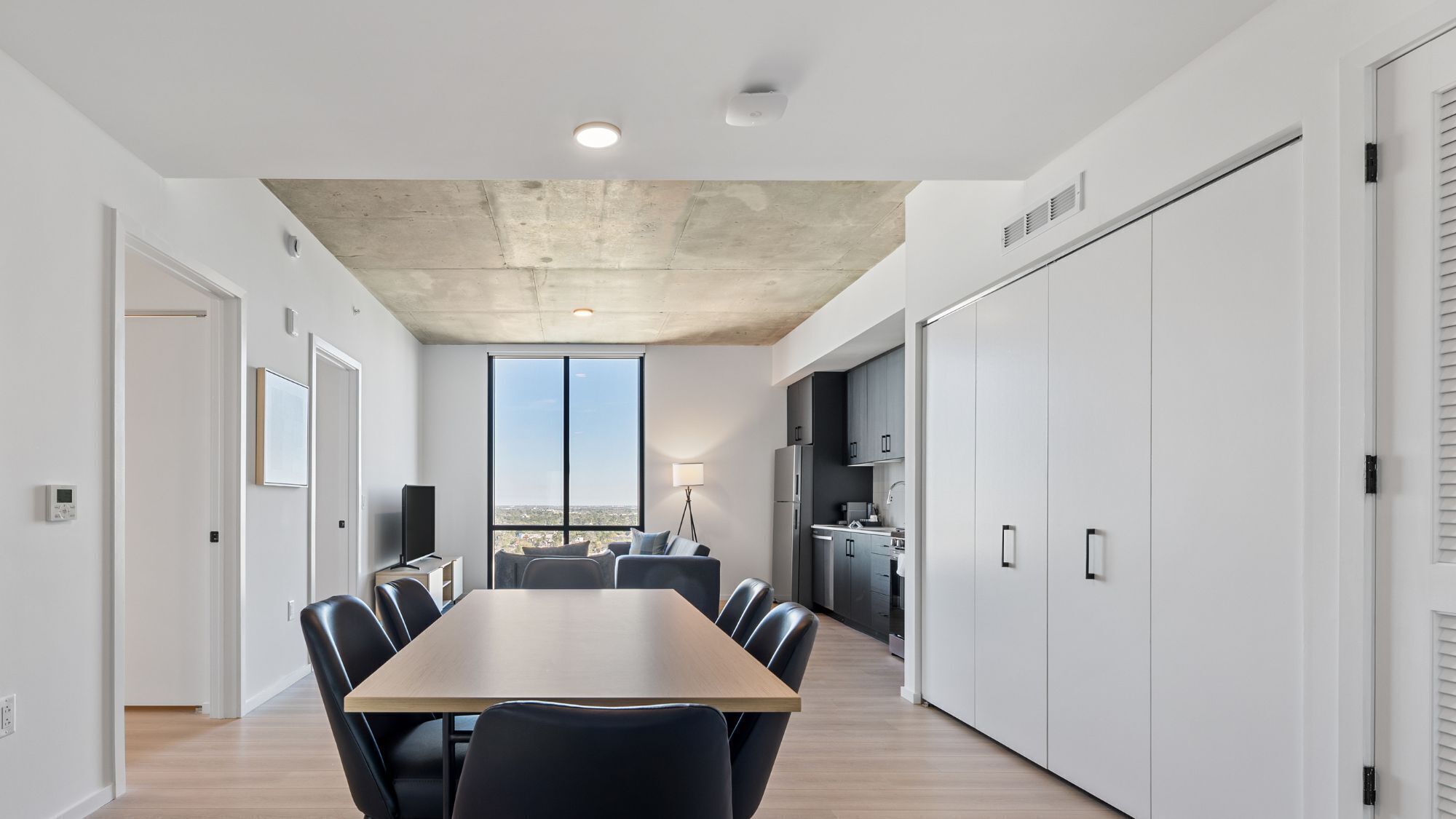 Un apartamento moderno con zona de comedor, cocina y ventanas amplias que ofrecen vistas a la ciudad.