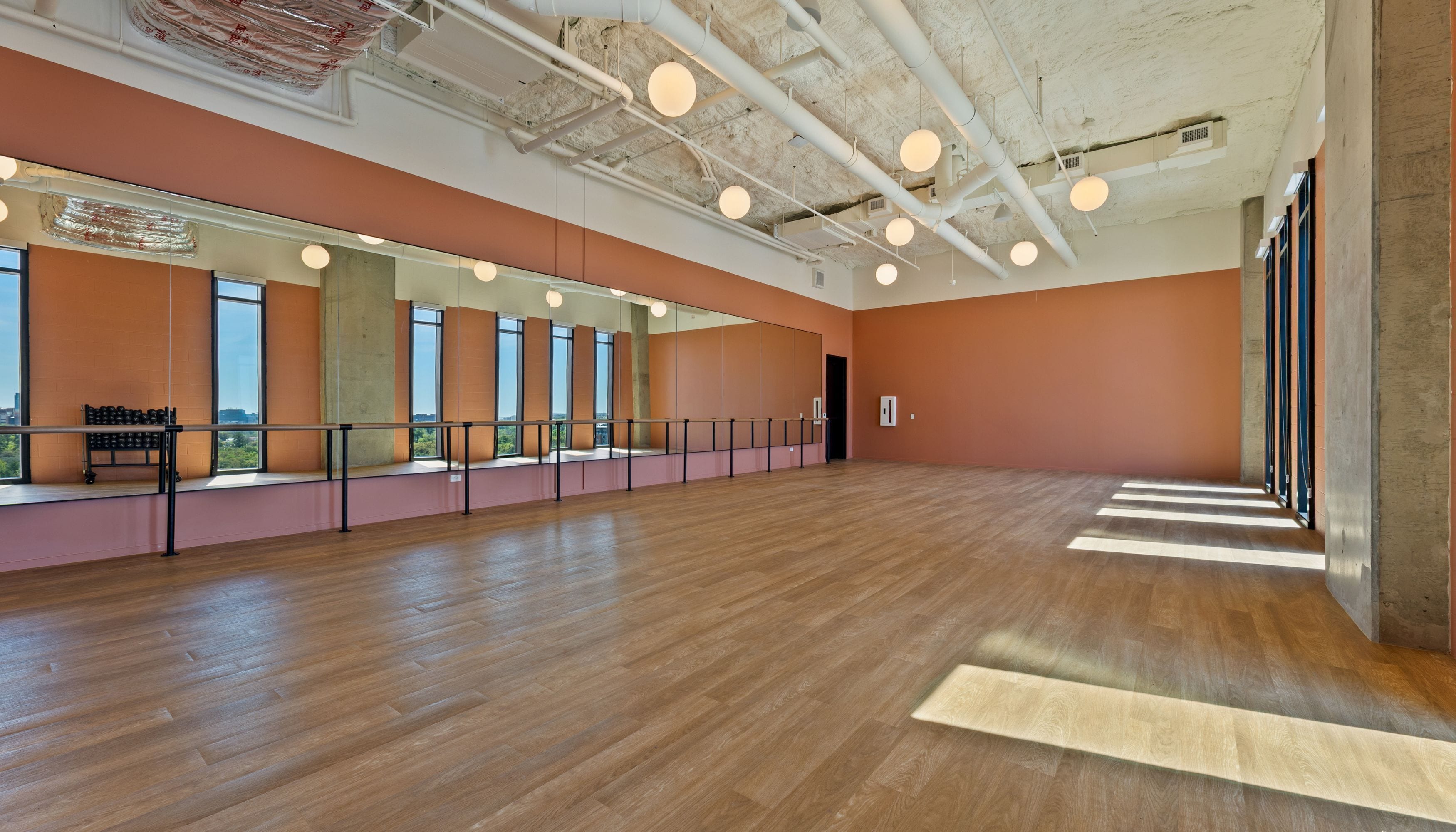 A spacious dance studio with a wooden floor, large windows, and a mirrored wall.