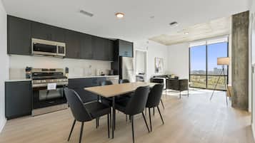 Una cocina moderna con armarios oscuros, electrodomésticos de acero inoxidable y un comedor con una mesa grande y sillas.