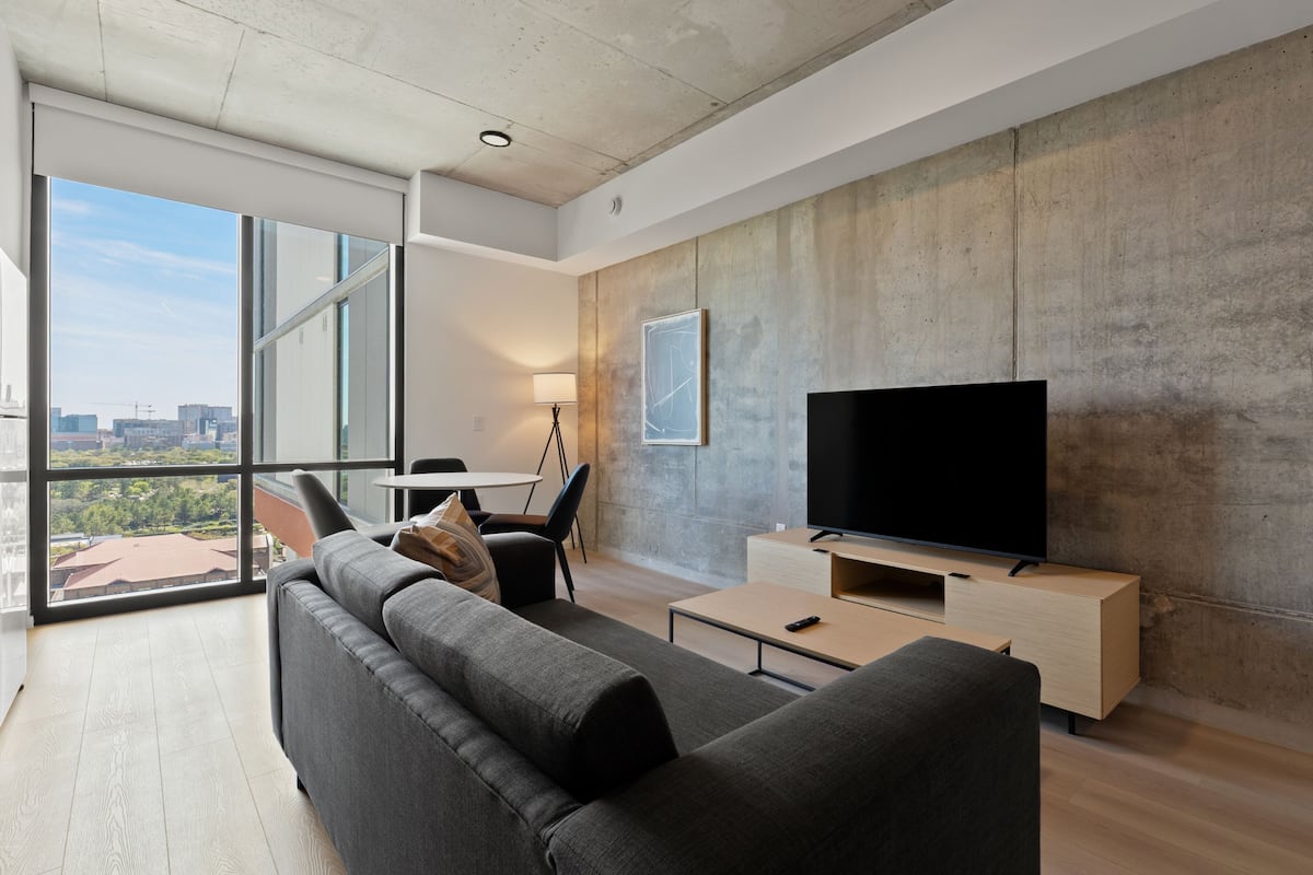Una sala de estar moderna con un ventanal grande, un televisor de pantalla plana, un sofá y una mesa de centro.