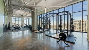 Ein großzügiger Fitnessraum mit großen Fenstern, Krafttrainingsgeräten und einem Betonboden.