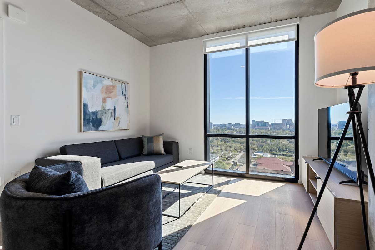 Una sala de estar moderna con un sofá, una mesa de centro, un televisor y un ventanal con vistas a la ciudad.
