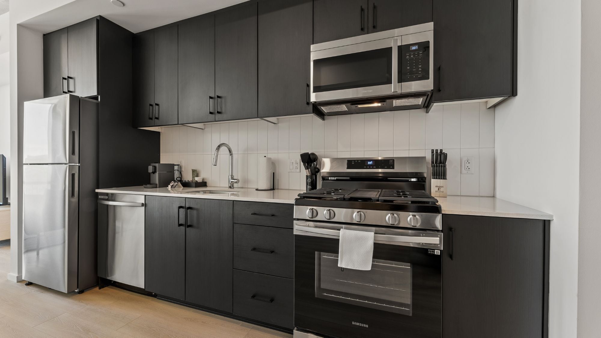 A modern kitchen with dark cabinetry, stainless steel appliances, and a white countertop.