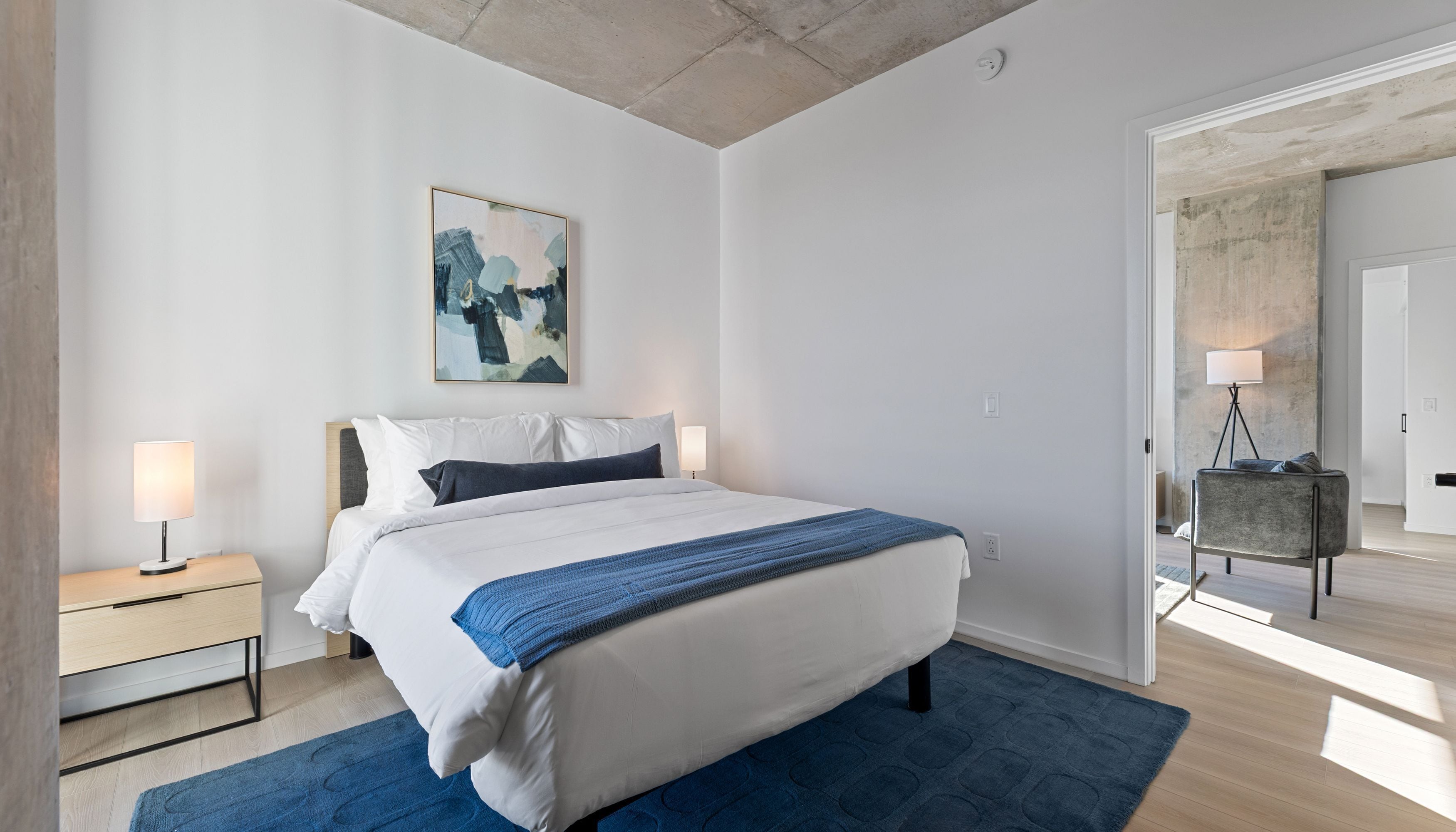 A modern bedroom with a bed, bedside tables, a floor lamp, and a painting on the wall.