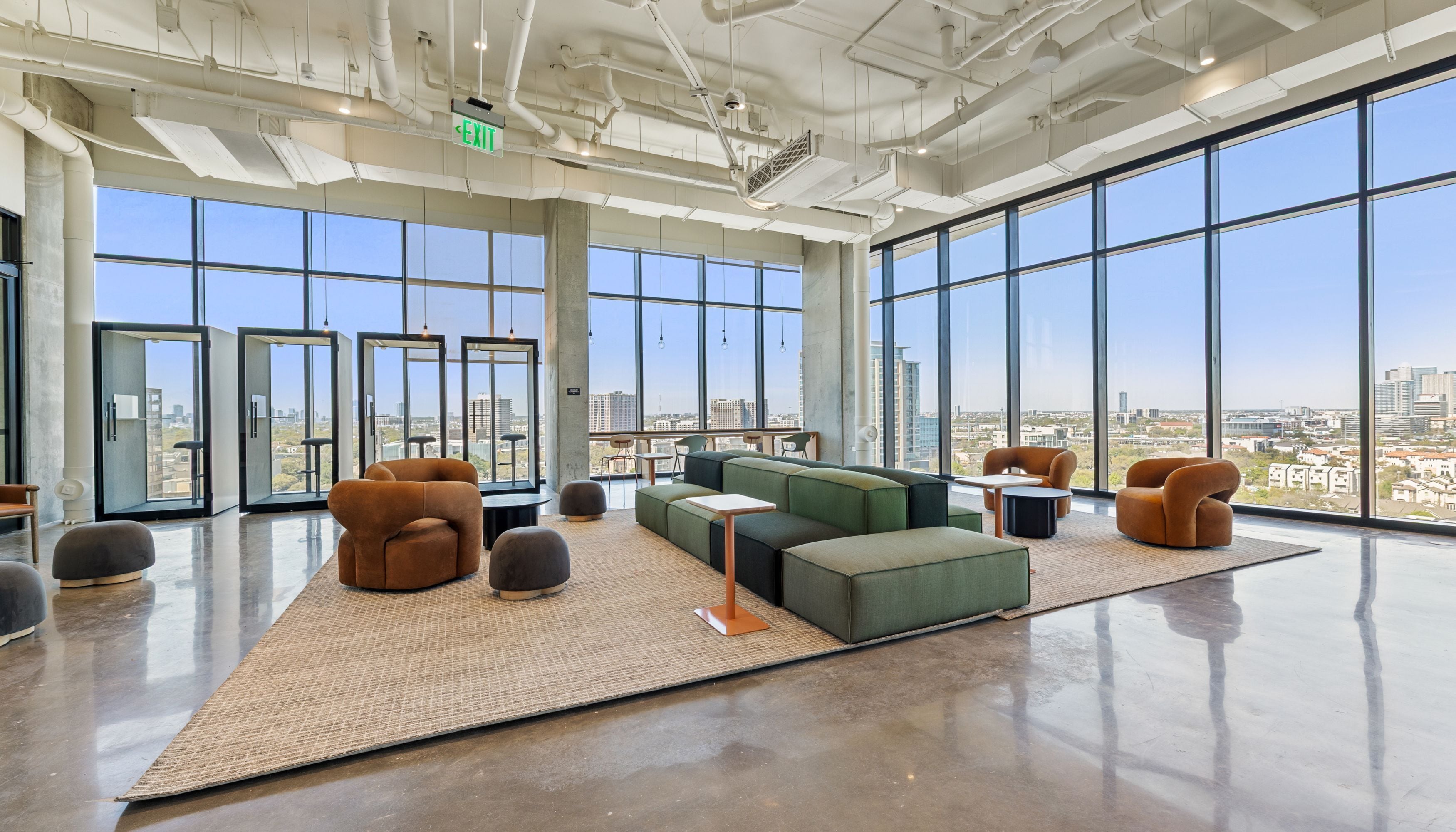 A spacious lounge with large windows, a green sofa, and a view of the cityscape.