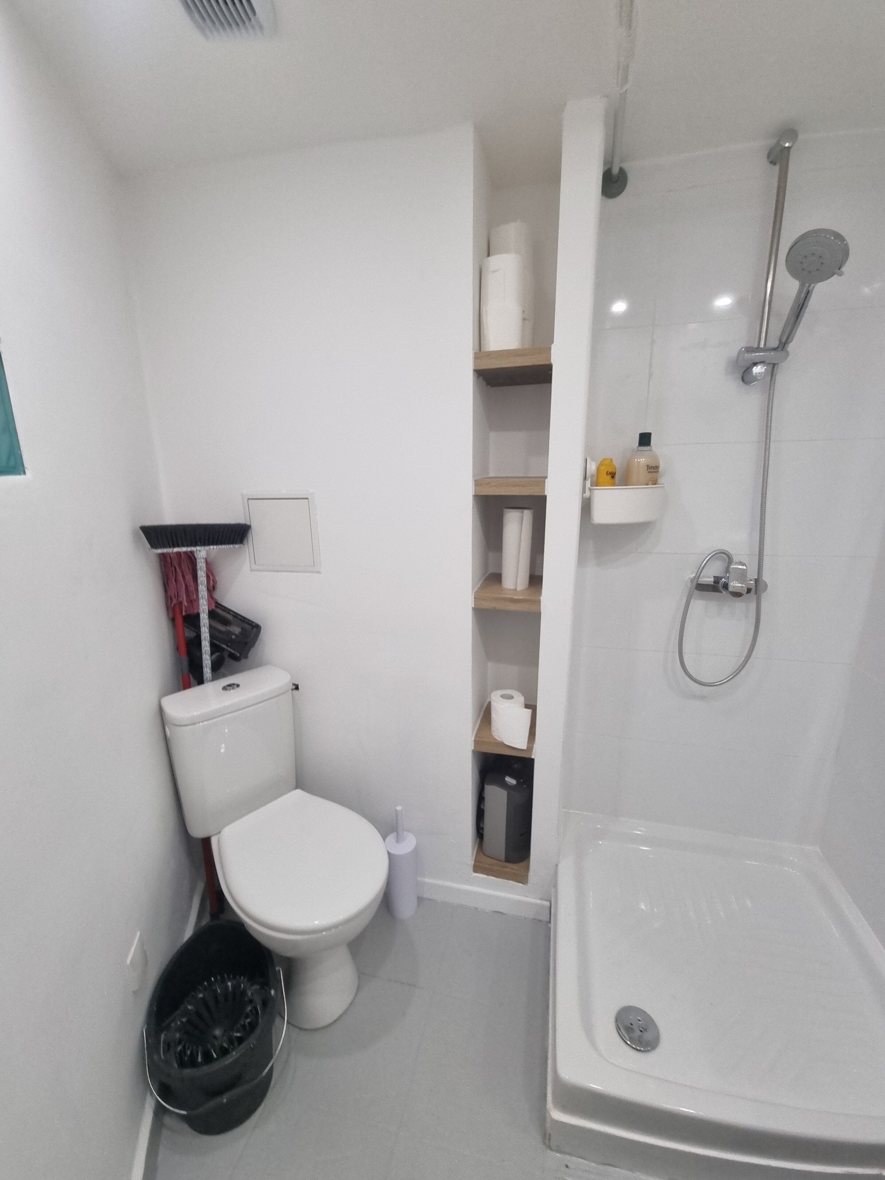 Une petite salle de bain comprenant des toilettes, une douche et une étagère avec des articles de toilette.