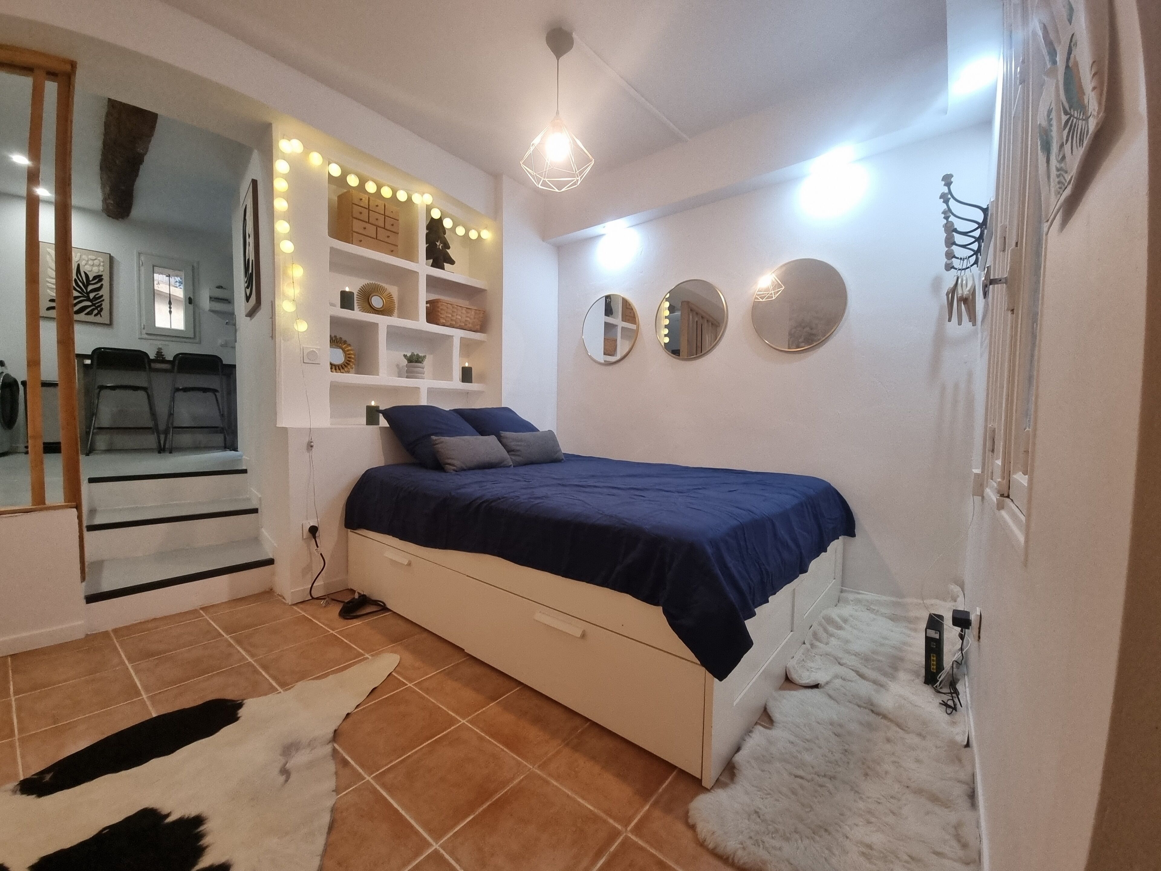 Une chambre à coucher comprenant un lit, une commode, un miroir et une étagère ornée d’objets décoratifs.