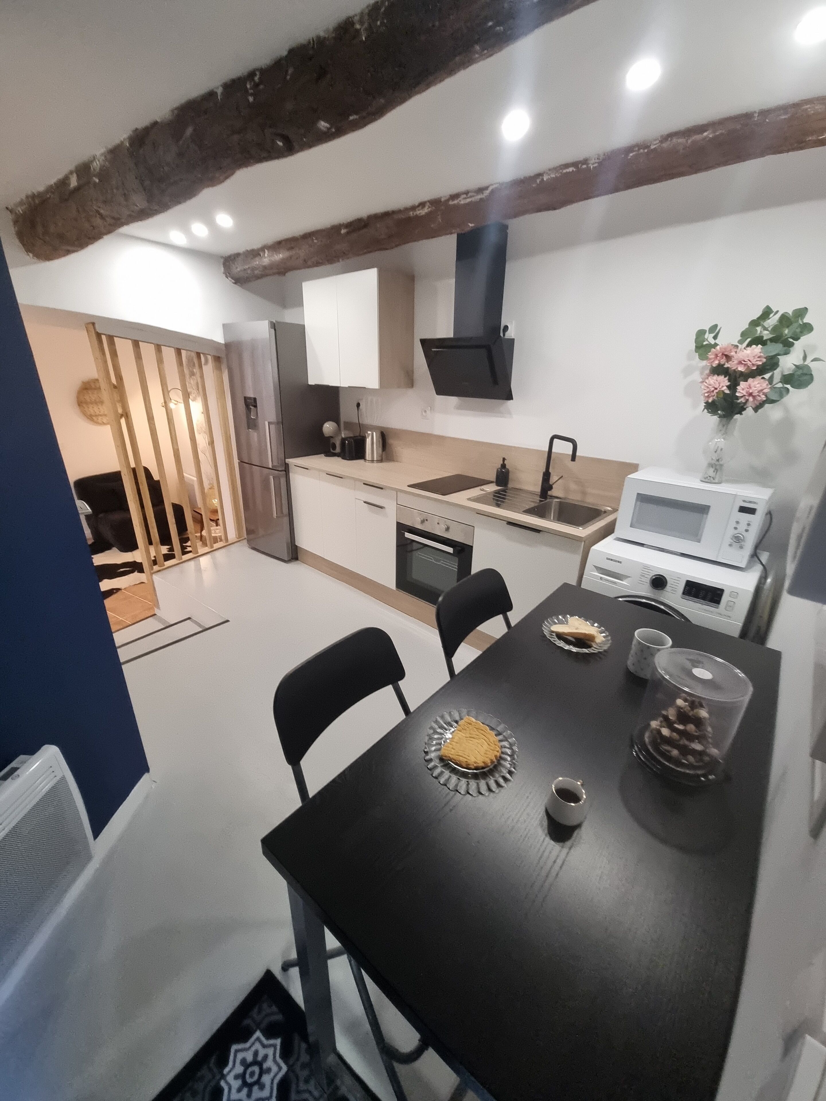Une cuisine moderne avec des meubles blancs, un plafond en bois et un coin repas comprenant une table et des chaises noires.