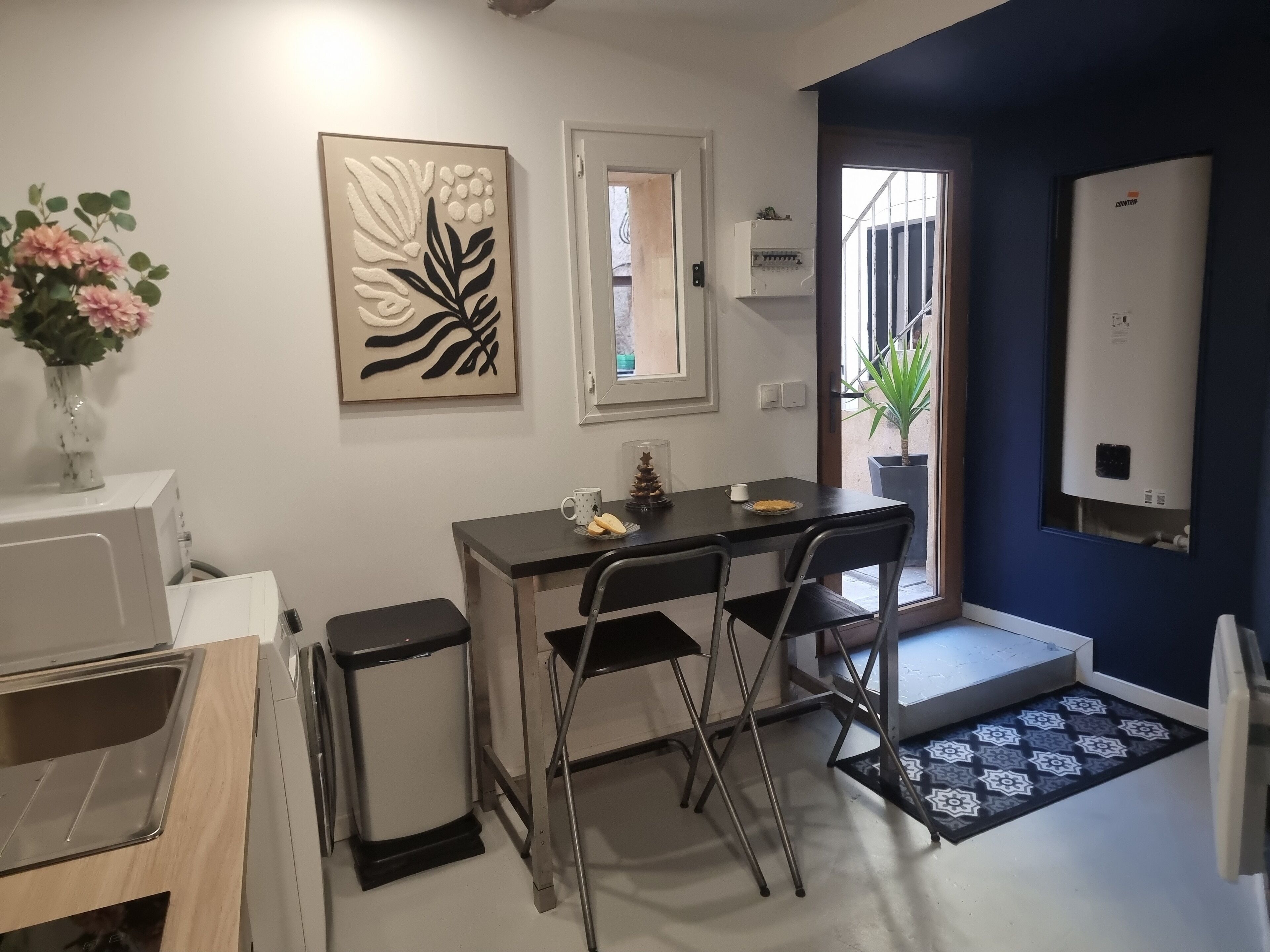 Une cuisine compacte avec un coin repas, un réfrigérateur blanc, une poubelle et une plante en pot.
