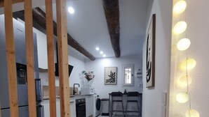 A modern kitchen with white cabinets, a wooden beam ceiling, and a dining area with two chairs and a table. - Renovated studio with private courtyard in the heart of Béziers (Béziers)