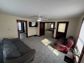 A living room with a grey sofa, a red sofa, a ceiling fan, and a TV mounted on the wall. - 3 bedroom 2 car garage near Lake Erie and cedar point great for large groups (Clyde)