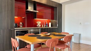 A modern kitchen with red cabinets, stainless steel appliances, and a wooden dining table with matching chairs.