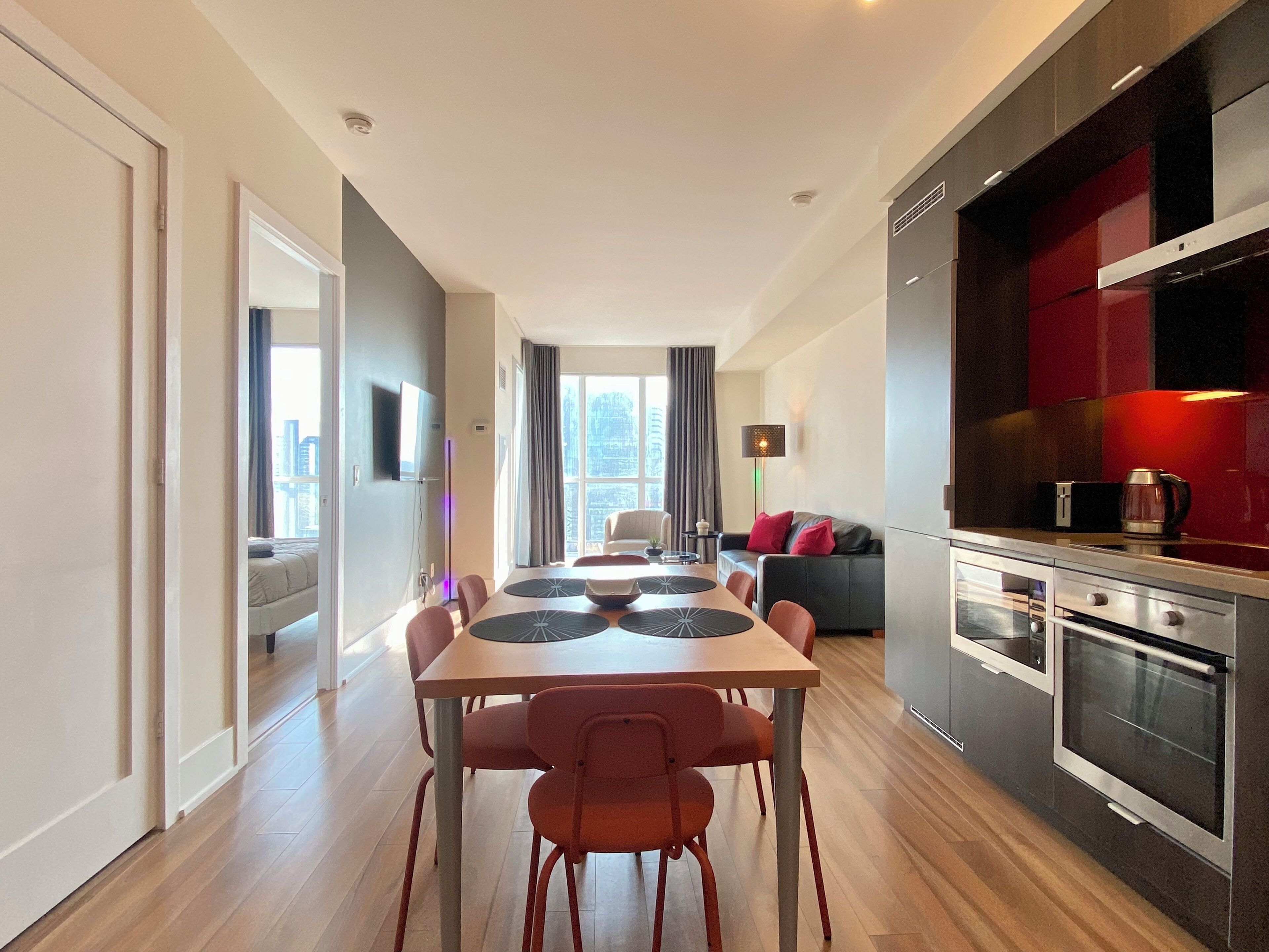 A modern kitchen with a dining area, featuring a large table with chairs, a sofa, and a TV mounted on the wall.