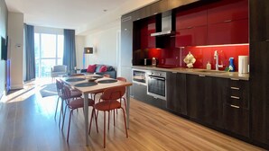 A modern kitchen with dark cabinetry, a red backsplash, and a dining area with a wooden table and red chairs.