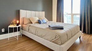 A modern bedroom with a large bed, a bedside table with a lamp, and a view of the city through a window.