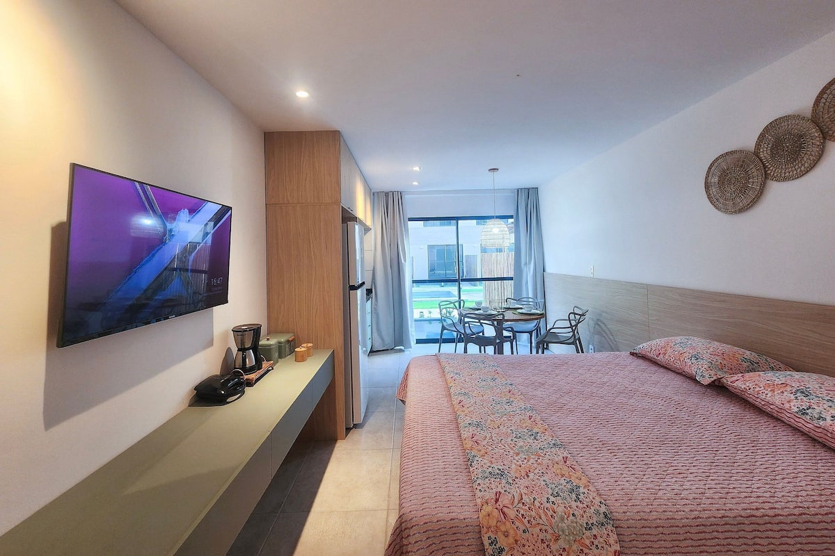 A modern hotel room with a bed, a TV, a desk, and a dining area.