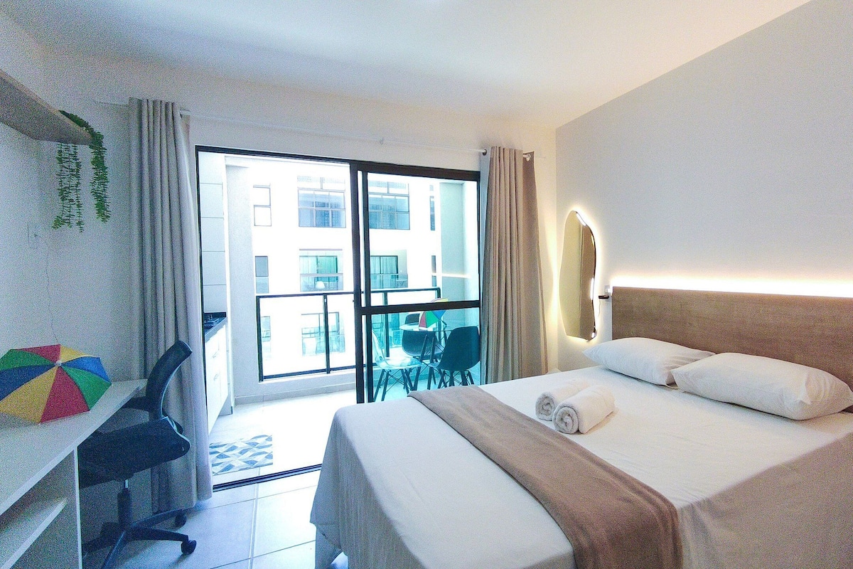 A hotel room with a bed, desk, chair, and a view of the outside.