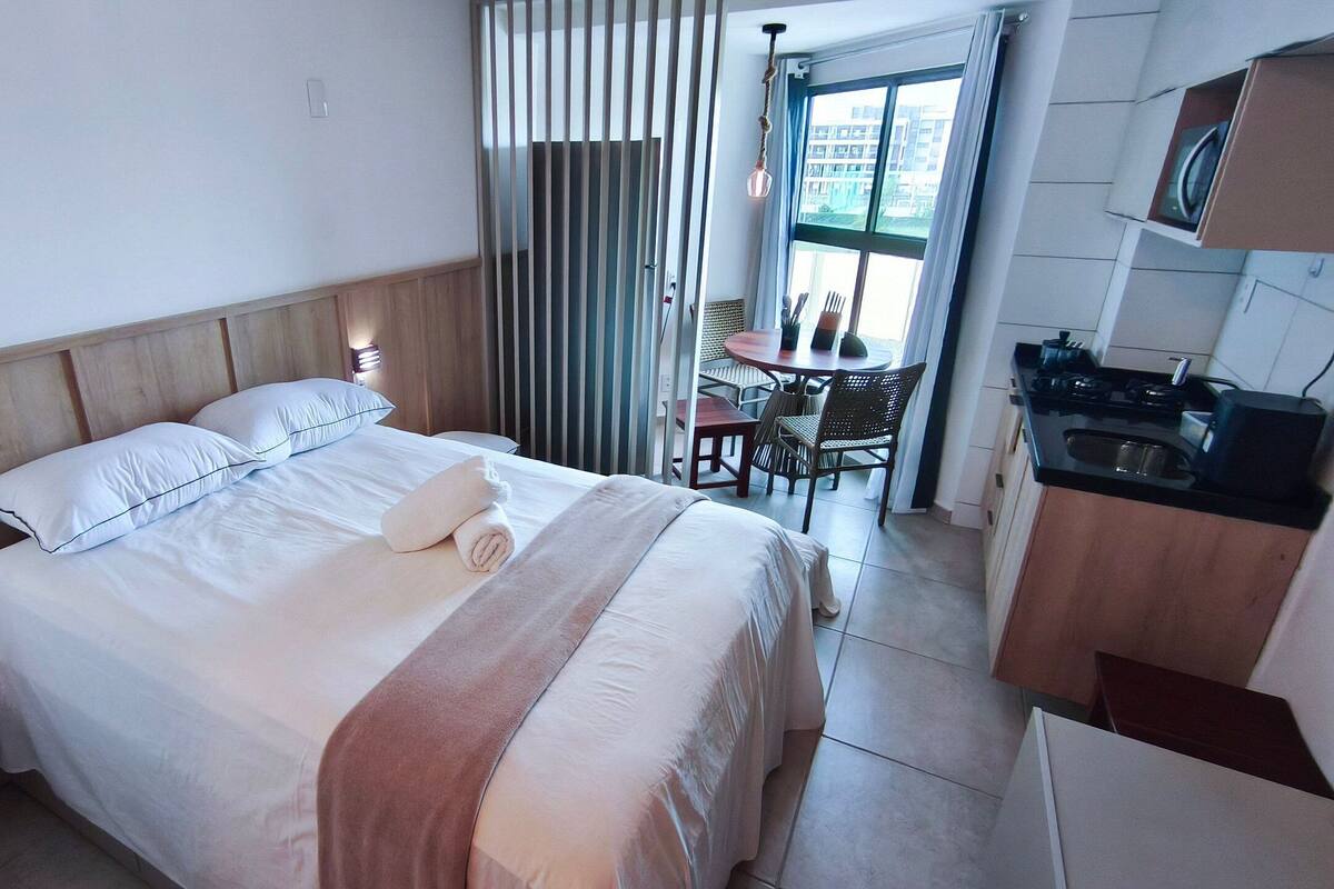 A hotel room with a bed, a desk, a chair, and a kitchenette.