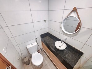A bathroom with a toilet, sink, mirror, and tiled walls. - Max Carneiros Suites - Praia dos Carneiros by CTA (Tamandaré)