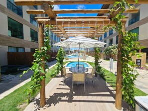An outdoor seating area with a pool, surrounded by wooden pergolas and greenery.