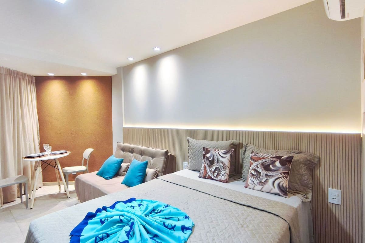 A modern hotel room with a bed, bedside table, and a small seating area with a chair and table.