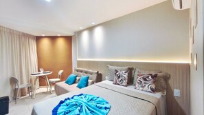 A modern hotel room with a bed, bedside table, and a small seating area with a chair and table. - Max Carneiros Suites - Praia dos Carneiros by CTA (Tamandaré)