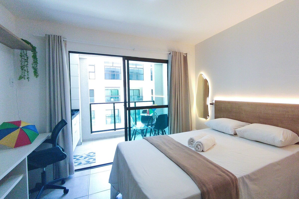 A hotel room with a bed, desk, chair, and a view of the outside.