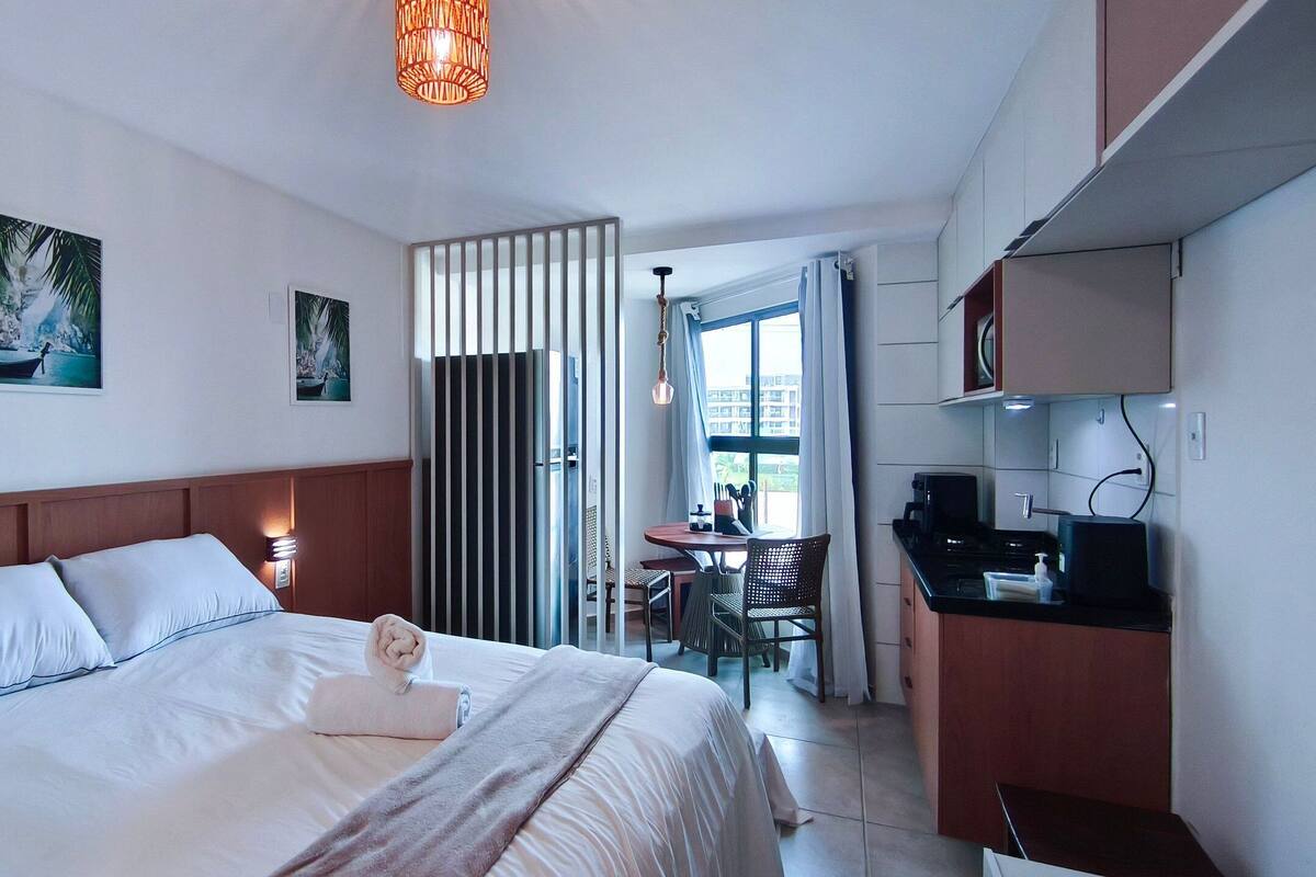 A hotel room with a bed, a desk, a chair, a dining table, and a kitchen area.