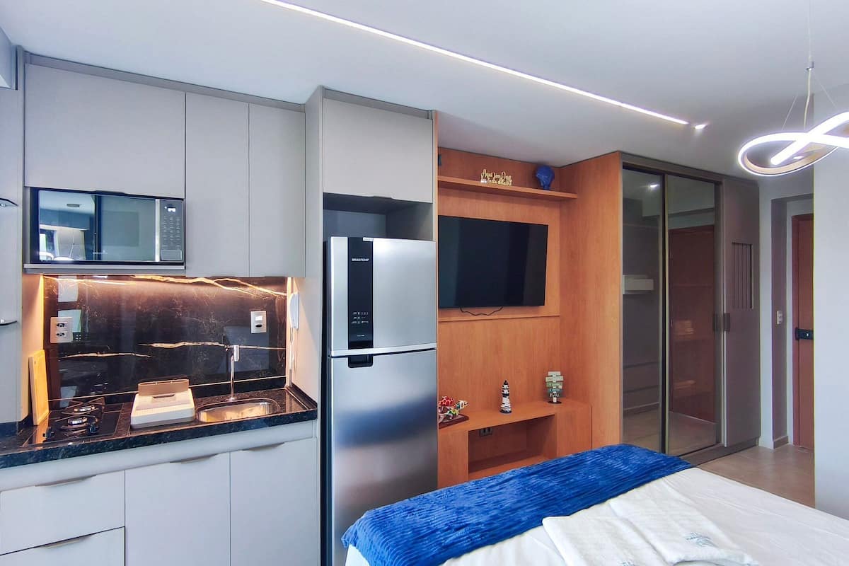 A modern kitchen with a built-in microwave, a stainless steel refrigerator, and a wooden shelf with decorative items.