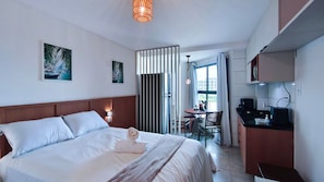 A hotel room with a bed, a desk, a chair, a dining table, and a kitchen area. - Max Carneiros Suites - Praia dos Carneiros by CTA (Tamandaré)