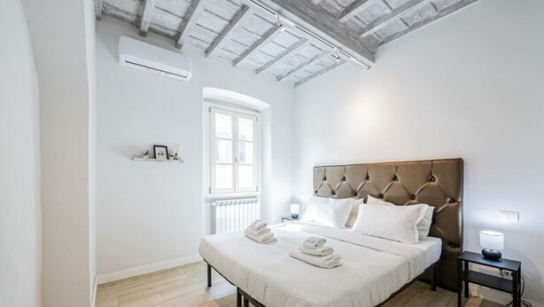 Une chambre avec un grand lit, un plancher en bois, une fenêtre et un plafond avec des poutres apparentes.