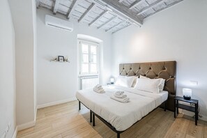 Une chambre avec un grand lit, un plancher en bois, une fenêtre et un plafond avec des poutres apparentes.