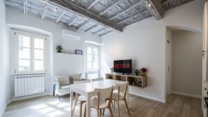 Un salon moderne avec une table blanche, des chaises en bois, un canapé et un téléviseur affichant le logo « NETFLIX ».